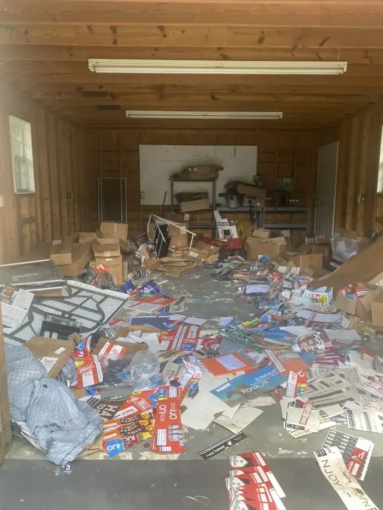 Auburn shed cleanout before - shed floor covered in boxes, signage, and household debris