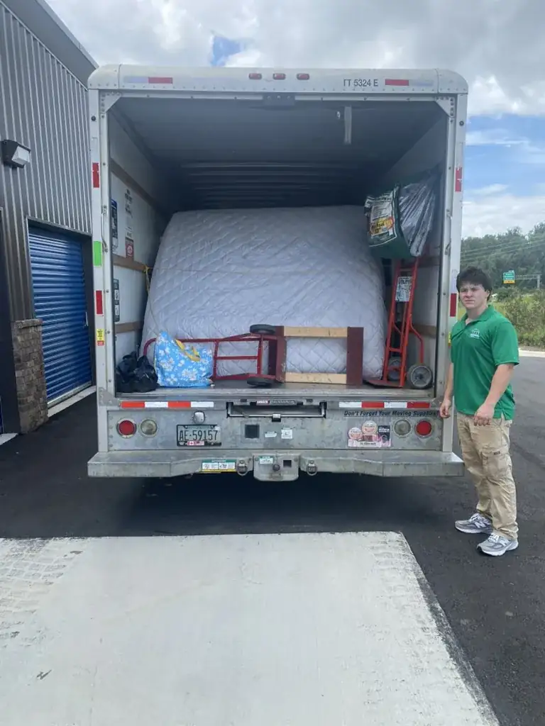 Toss It crew member standing beside a loaded U-Haul truck full of mattresses and furniture during a removal job in Auburn, Alabama